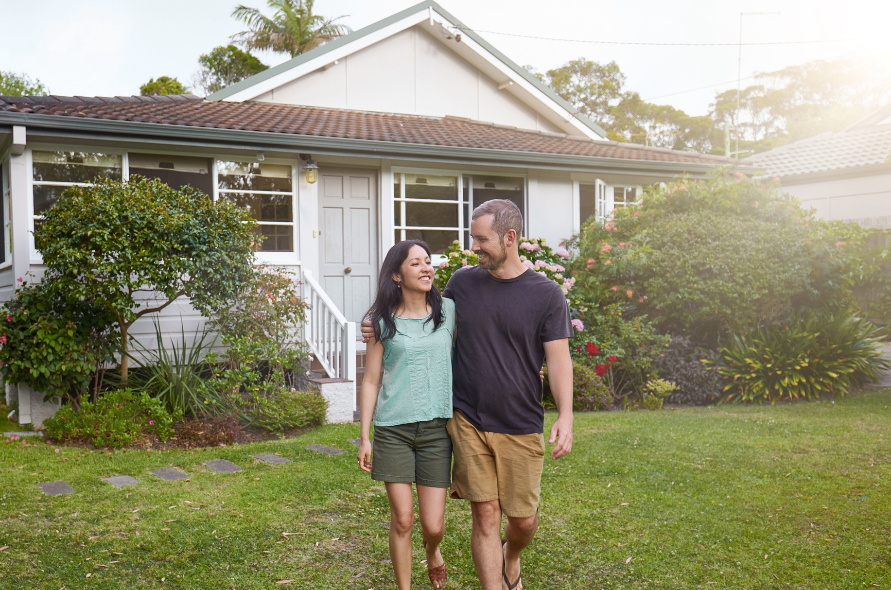 Happy mixed-race couple walking outside their front yard garden.