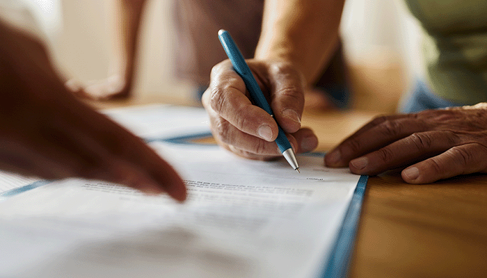 A close-up of someone signing a piece of paper with a blue pen on a table.