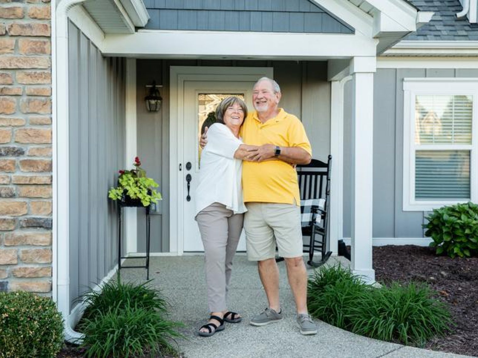 An older couple hugging outside the home they just refinanced.