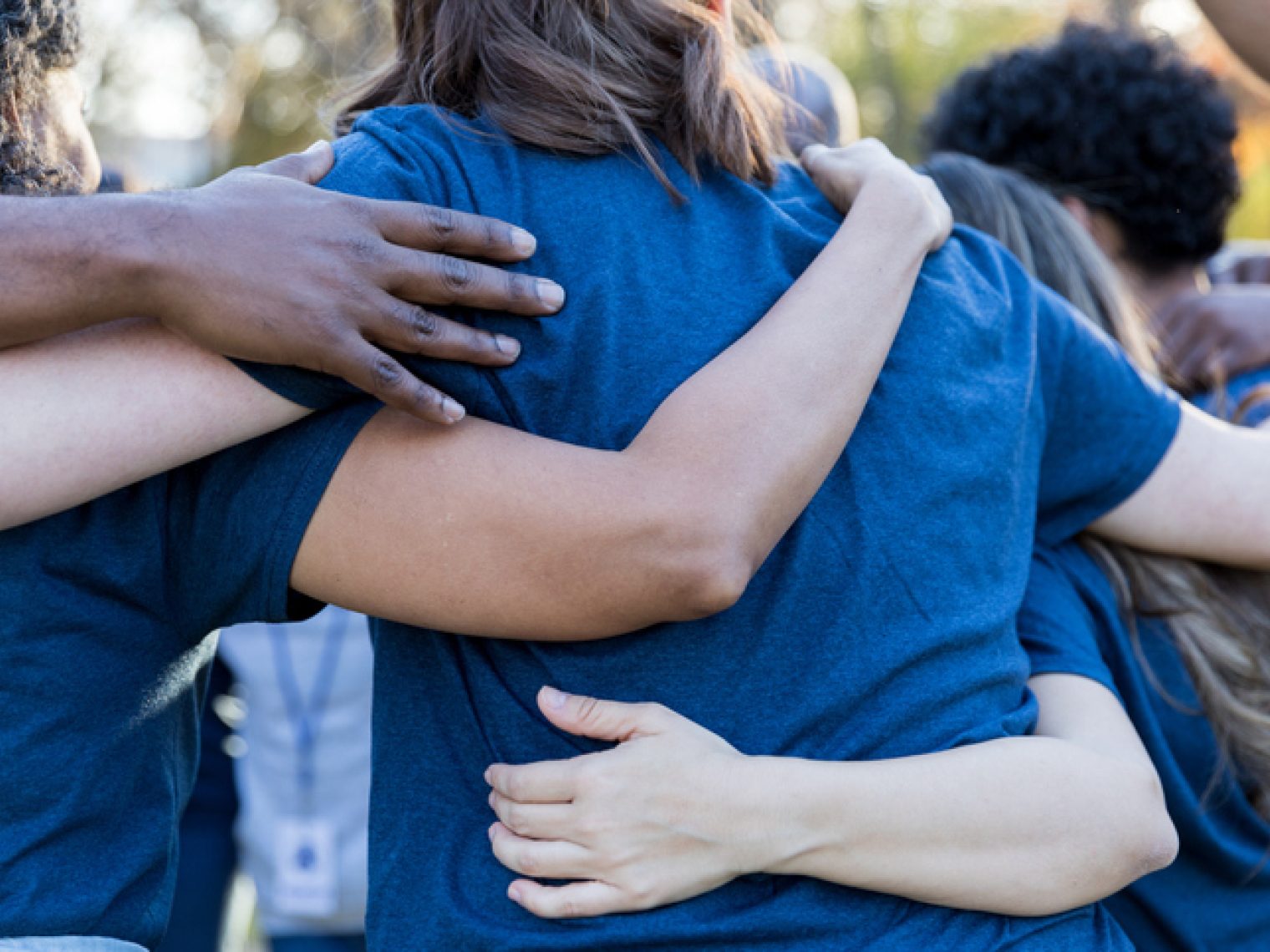 A close-up of a diverse group of people in blue shirts, embracing each other in a supportive huddle.