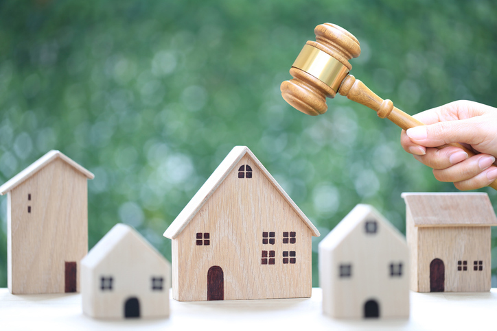 A hand holding a wooden auctioneer's gavel above miniature house models, symbolizing real estate auction.