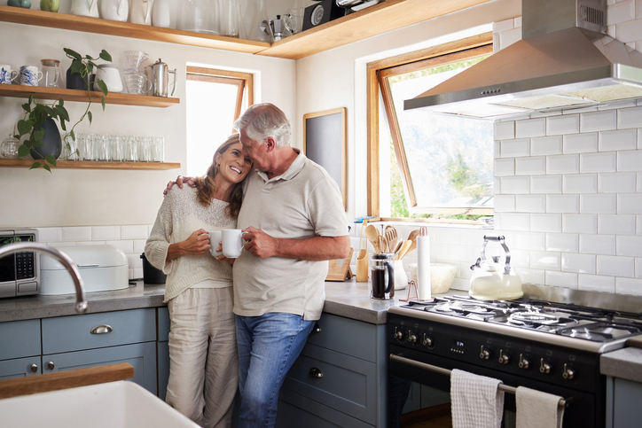 An affectionate couple shares a cozy moment in a well-lit kitchen with a cup of coffee, surrounded by modern appliances and decor.