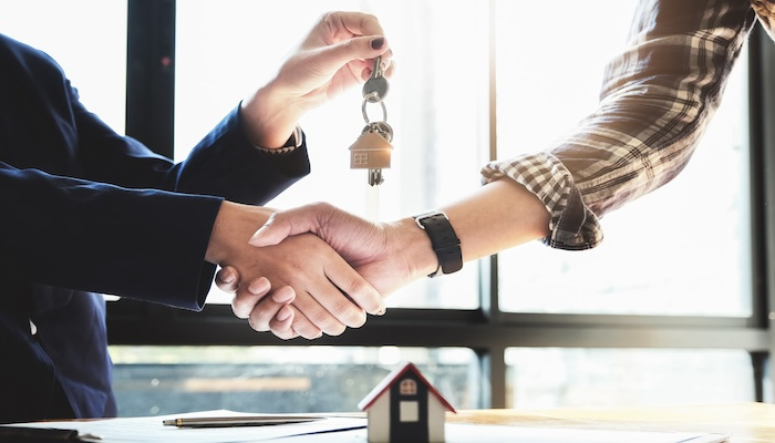 Real estate agent shakes homebuyer's hand while handing him house keys.