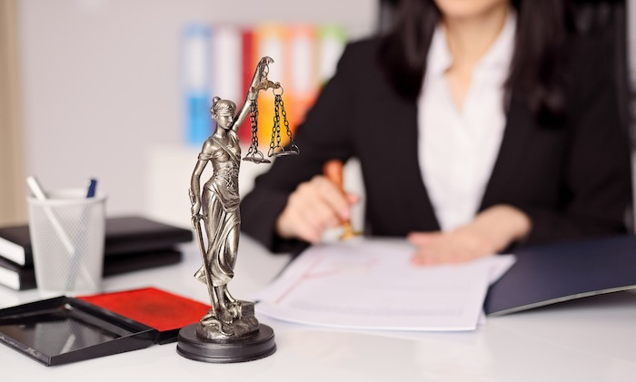 Small statue of goddess of justice on a lawyer's desk while she stamps a legal document.