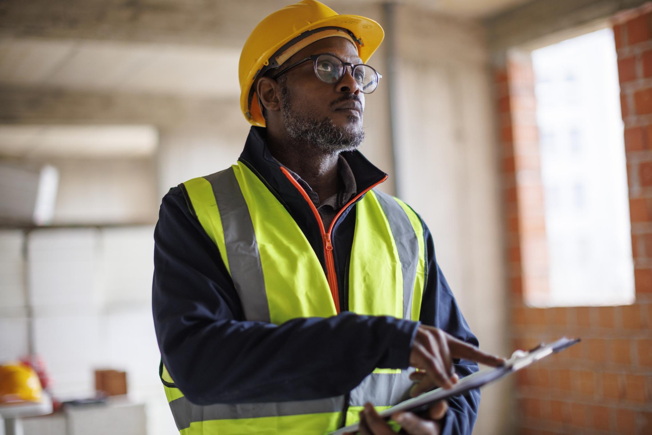 A man wearing a yellow vest and hard hat doing a radon test in the home.