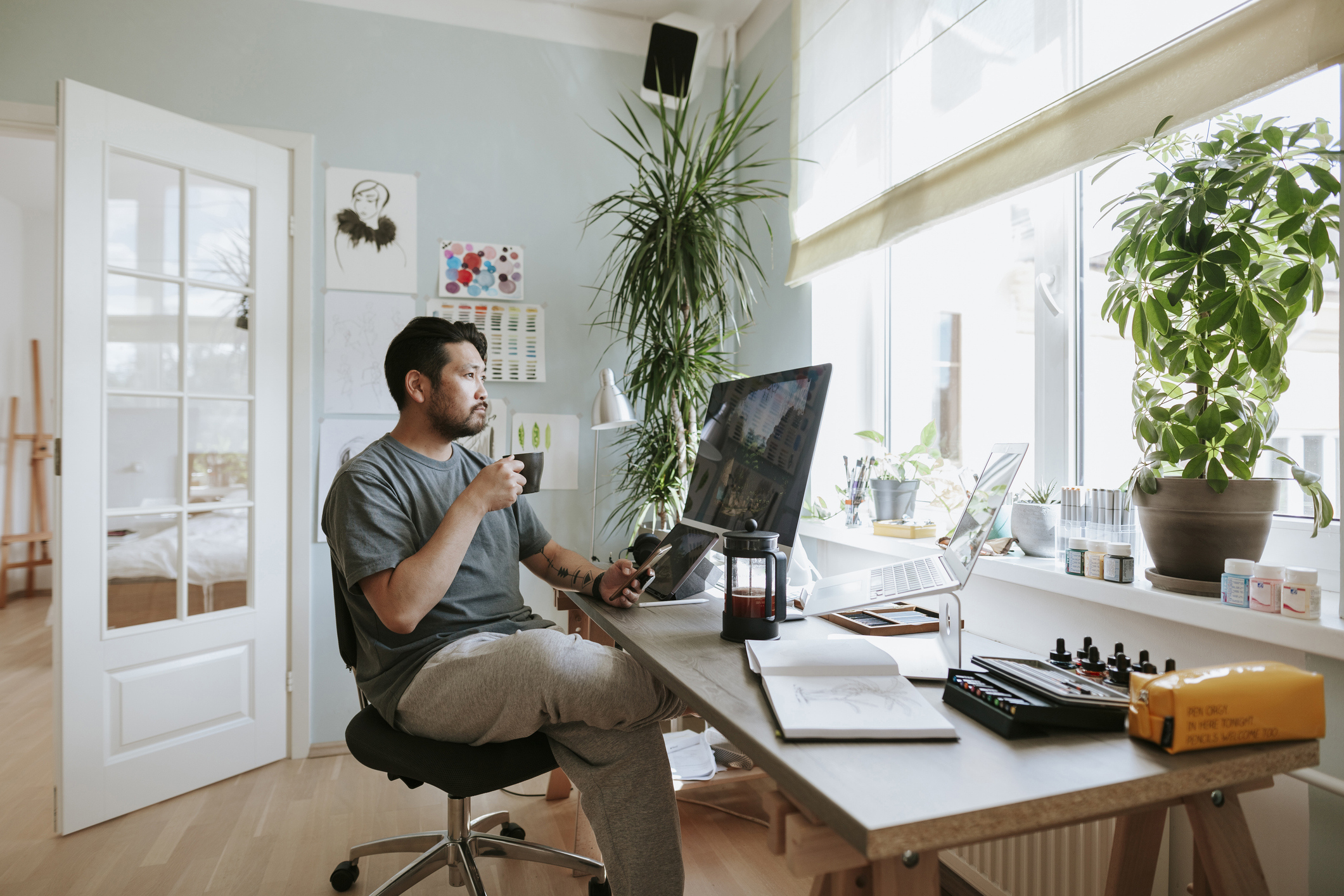 Man holding coffee in hand sitting at desk with a pensive look on his face.